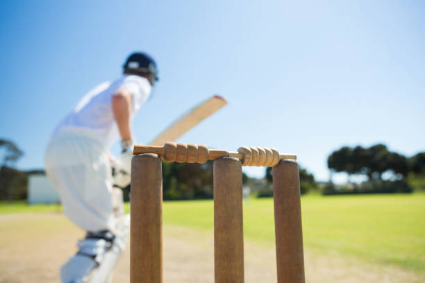 Close up of wooden stump by batsman standing on field against clear sky